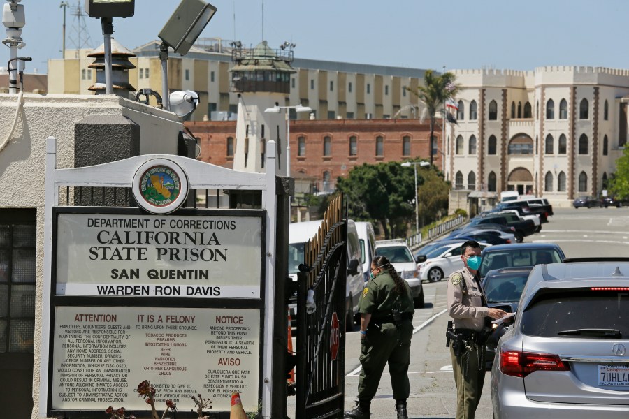 In this July 9, 2020 file photo a correctional officer checks a car entering the main gate of San Quentin State Prison, in San Quentin, Calif. (AP Photo/Eric Risberg,File)