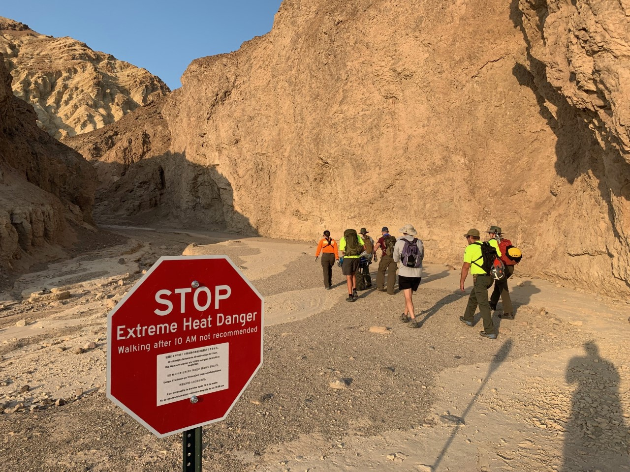 In this Wednesday, Aug. 18, 2021, photo provided by the National Park Service, an inter-agency search and rescue crew walks past a sign reading" "Stop, Extreme Heat Danger," with park rangers responding on foot near Red Cathedral along the Golden Canyon Trail in Death Valley National Park, Calif. (National Park Service via AP)