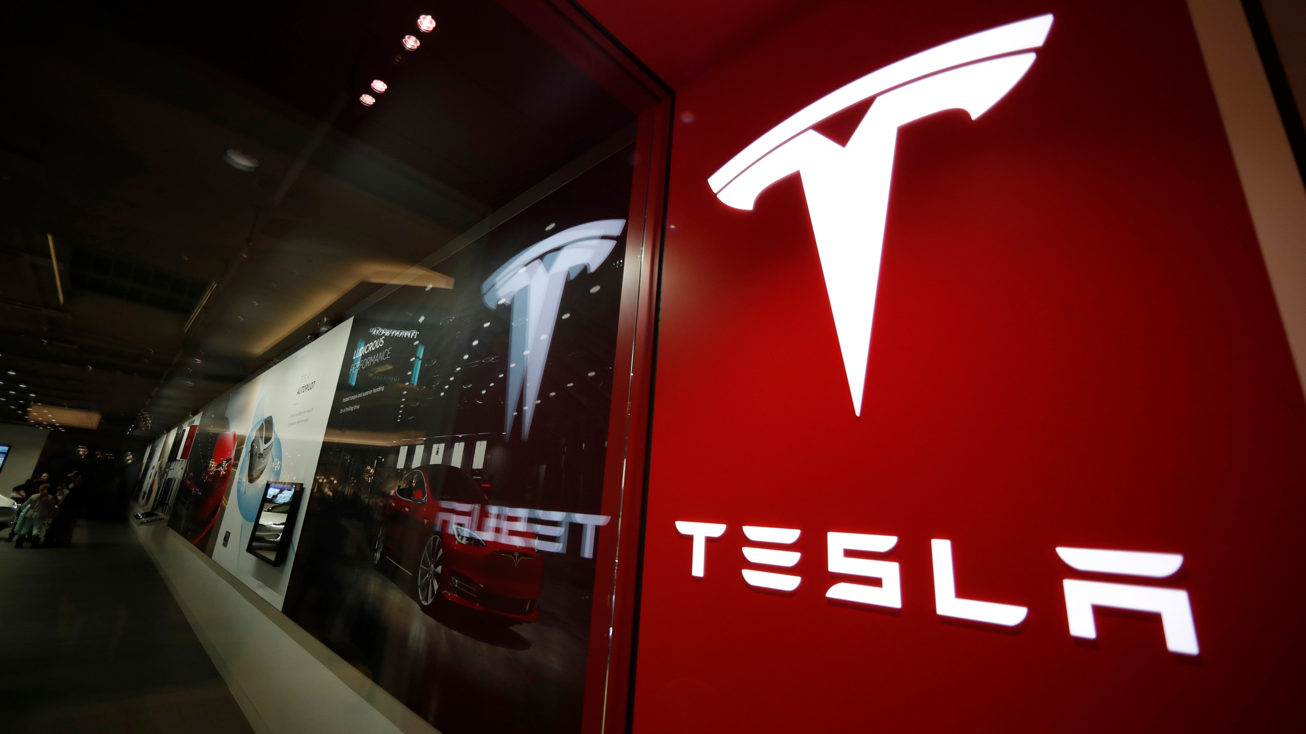 This Feb. 9, 2019, file photo shows a sign bearing the company logo outside a Tesla store in Cherry Creek Mall in Denver. A Tesla using its partially automated driving system slammed into a Florida Highway Patrol cruiser Saturday, Aug. 28, 2021 on an interstate near downtown Orlando and narrowly missed its driver, who had pulled over to assist a disabled vehicle. (AP Photo/David Zalubowski, File)