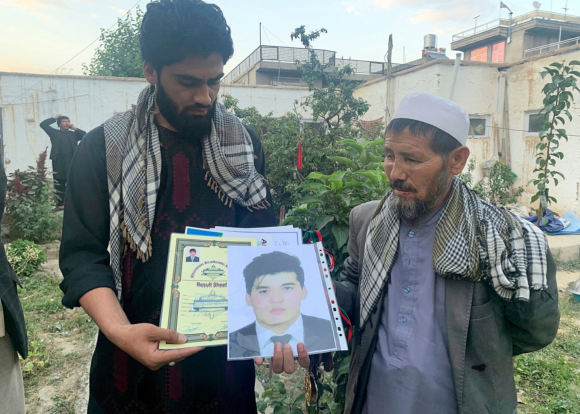 Mohammed Jan Sultani's father, Ali, right, looks at his son's Taekwondo championship certificates along with picture of him during an interview with The Associated Press in Kabul, Afghanistan, Sunday, Aug. 29, 2021. Mohammed Jan Sultani had clutched his national Taekwondo championship certificates as he waded through the multitudes pushing to get into Kabul airport late last week. (AP Photo/Kathy Gannon)