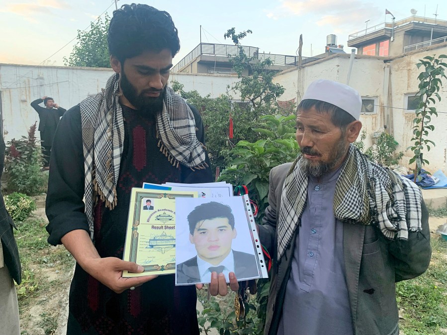 Mohammed Jan Sultani's father, Ali, right, looks at his son's Taekwondo championship certificates along with picture of him during an interview with The Associated Press in Kabul, Afghanistan, Sunday, Aug. 29, 2021. Mohammed Jan Sultani had clutched his national Taekwondo championship certificates as he waded through the multitudes pushing to get into Kabul airport late last week. (AP Photo/Kathy Gannon)