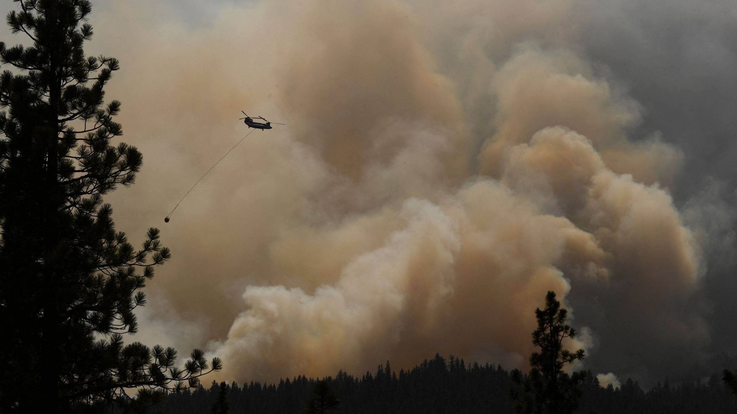 A firefighting helicopter flies past smoke plumes after making a water drop during the Dixie Fire on Aug. 18, 2021 near Susanville, California. (PATRICK T. FALLON/AFP via Getty Images)