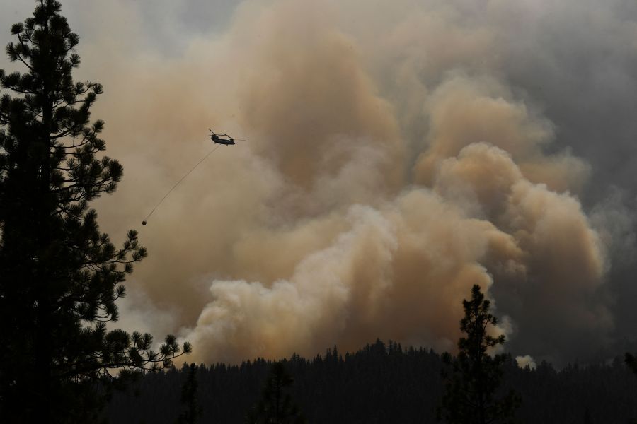 A firefighting helicopter flies past smoke plumes after making a water drop during the Dixie Fire on Aug. 18, 2021 near Susanville, California. (PATRICK T. FALLON/AFP via Getty Images)