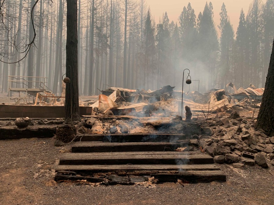 Smoke comes out under the front steps of a house that burned along North Arm Road in Plumas County near Taylorsville, Calif., Sunday, Aug. 15, 2021. (AP Photo/Eugene Garcia)