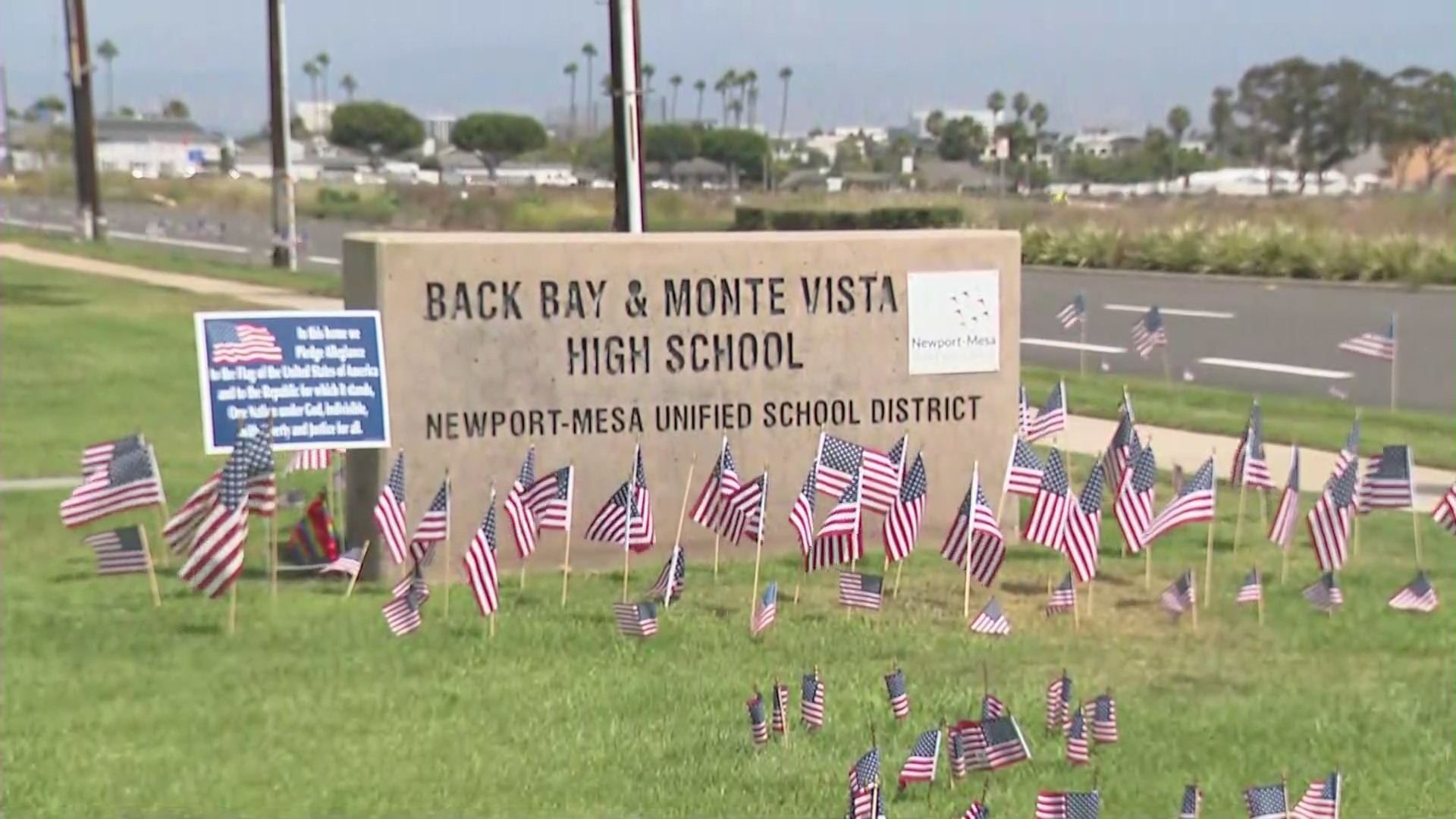 A sign outside Back Bay and Monte Vista high schools, which share a campus, is surrounded by American flags and at least one pride flag on Aug. 31, 2021, amid a controversy over a teacher's TikTok video. (KTLA)