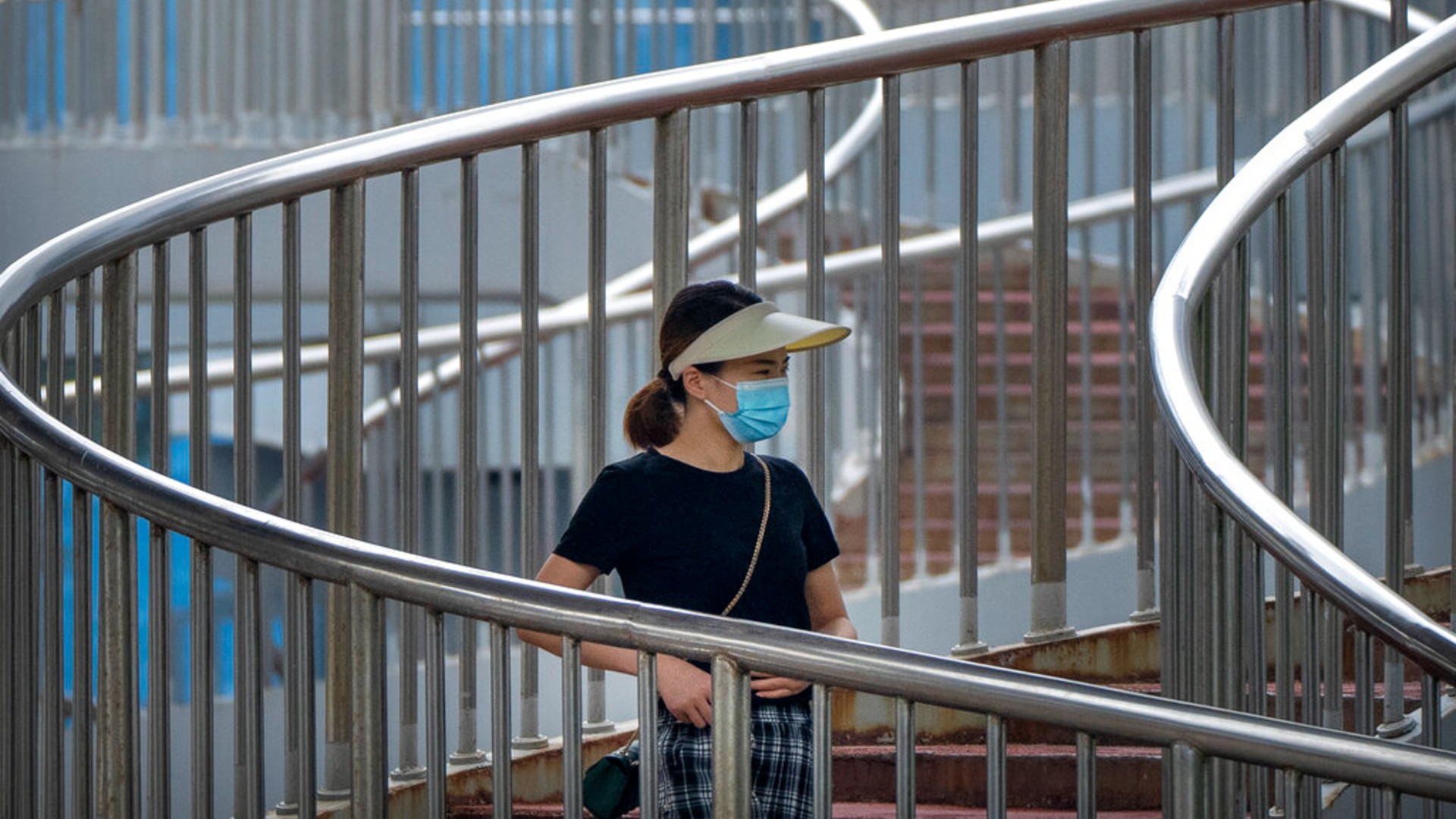 A woman wearing a face mask to protect against COVID-19 walk across a pedestrian bridge during the morning rush hour in Beijing, Wednesday, Aug. 4, 2021. (AP Photo/Mark Schiefelbein)