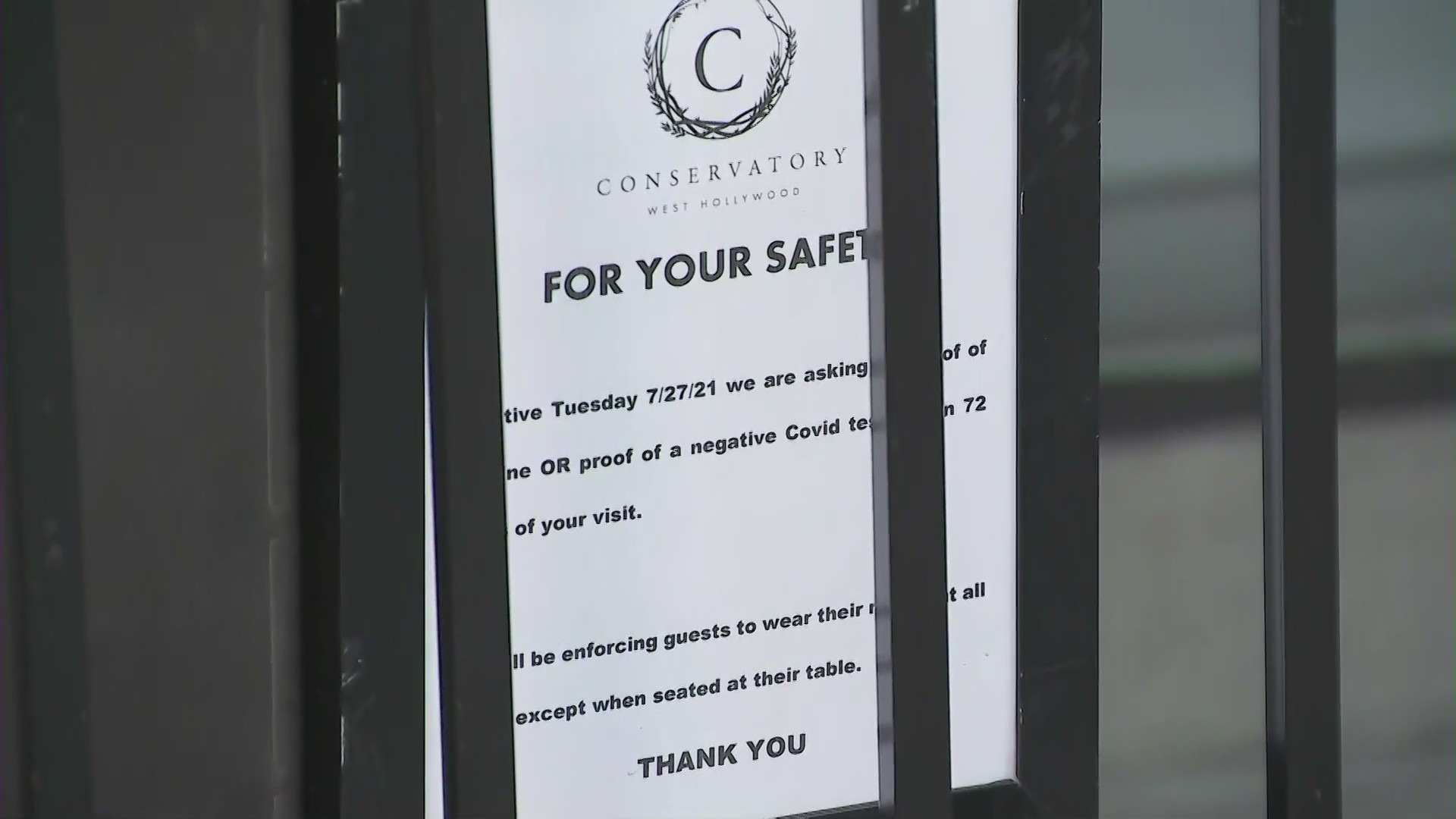 A sign asking customers for proof of vaccine or a negative coronavirus test is seen outside the Conservatory in West Hollywood on Aug. 2, 2021. (KTLA)