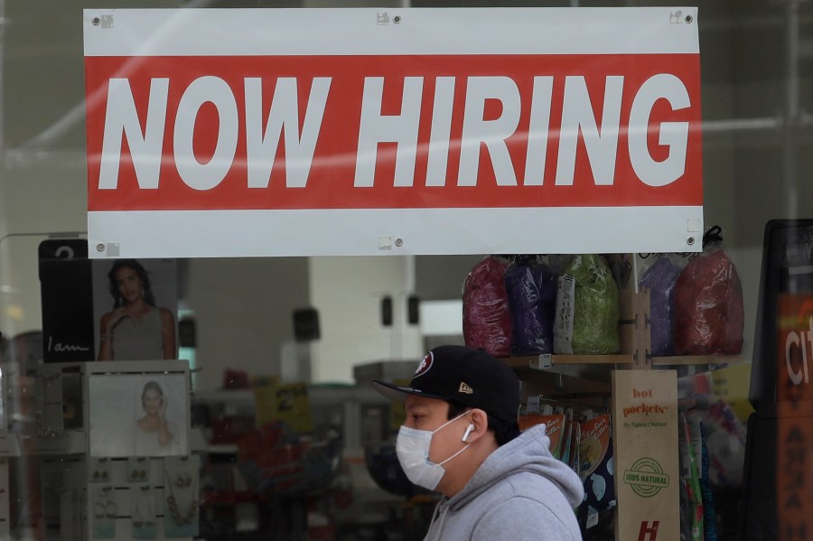 This May 7, 2020, file photo shows a man wearing a mask while walking under a Now Hiring sign at a CVS Pharmacy during the coronavirus outbreak in San Francisco. (AP Photo/Jeff Chiu, File)