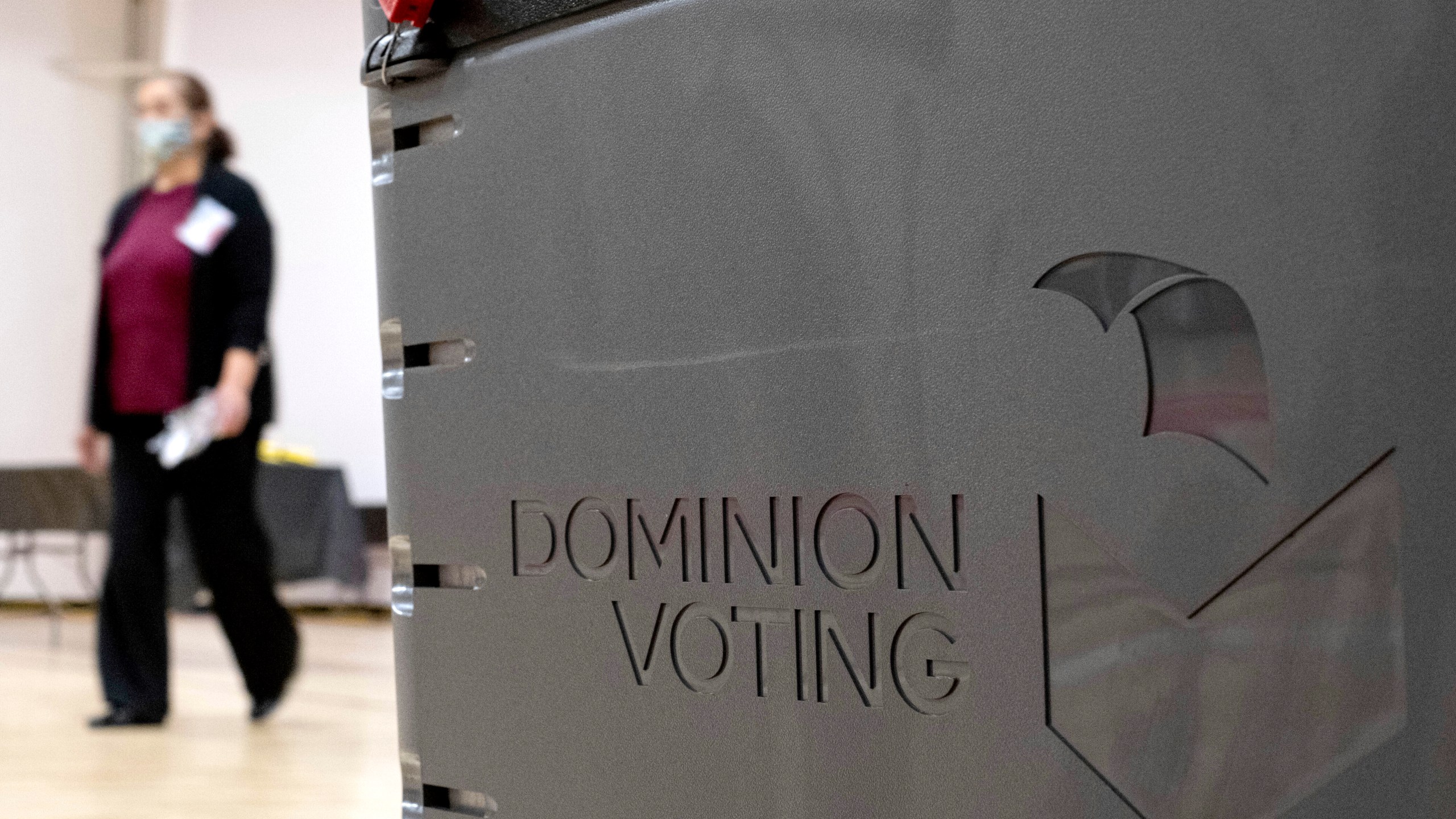 In this Jan. 4, 2021, file photo a worker passes a Dominion Voting ballot scanner while setting up a polling location at an elementary school in Gwinnett County, Ga., outside of Atlanta. A group of election security experts will ask California officials, Thursday, Sept. 2, to take additional steps to protect the upcoming governor’s recall election after the unauthorized release of voting system software in other states. (AP Photo/Ben Gray, File)