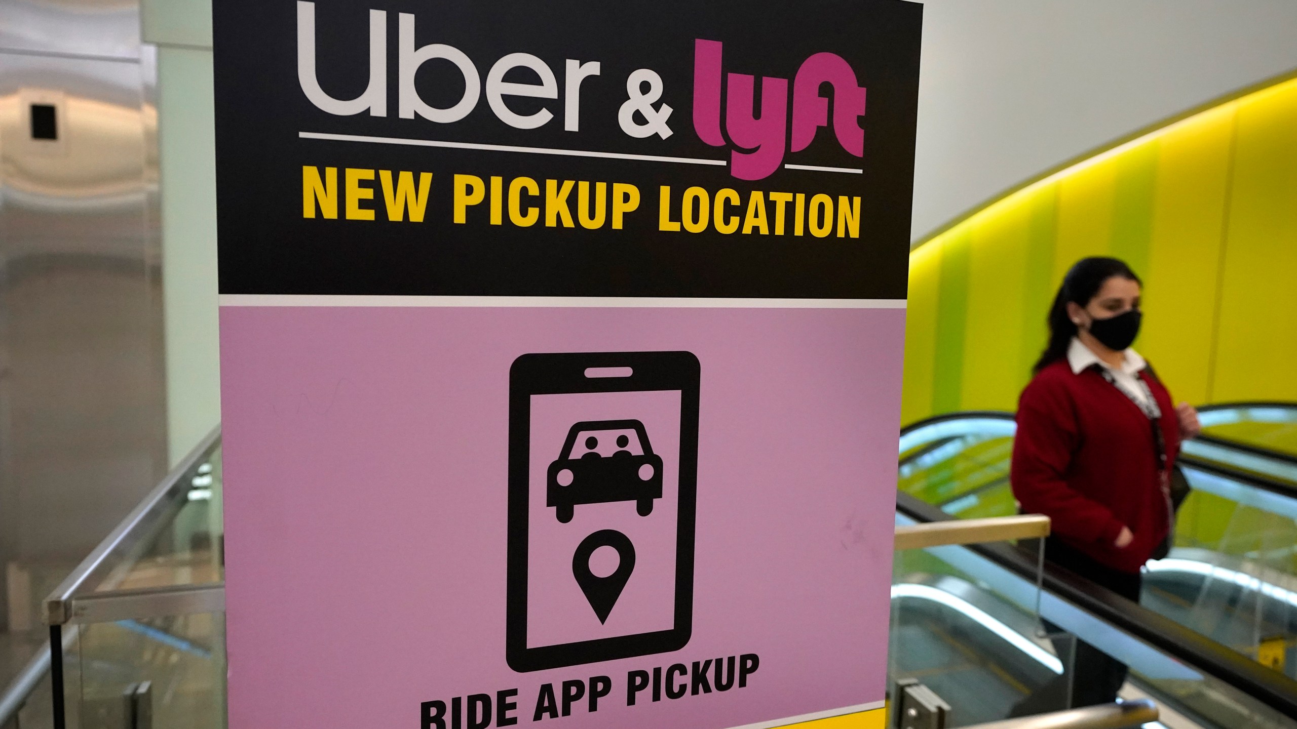 In this Feb. 9, 2021, file photo, a passer-by walks past a sign offering directions to an Uber and Lyft ride pickup location at Logan International Airport, in Boston. (AP Photo/Steven Senne, File)