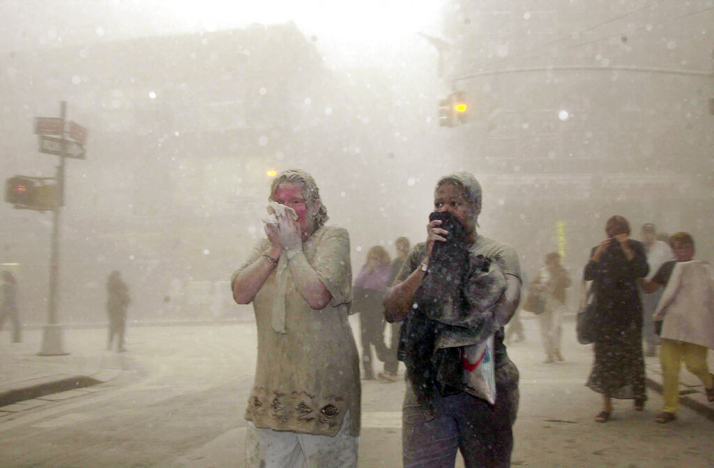 In this Sept. 11, 2001 file photo, people covered in dust from the collapsed World Trade Center buildings, walk through the area, in New York. (AP Photo/Suzanne Plunkett, File)