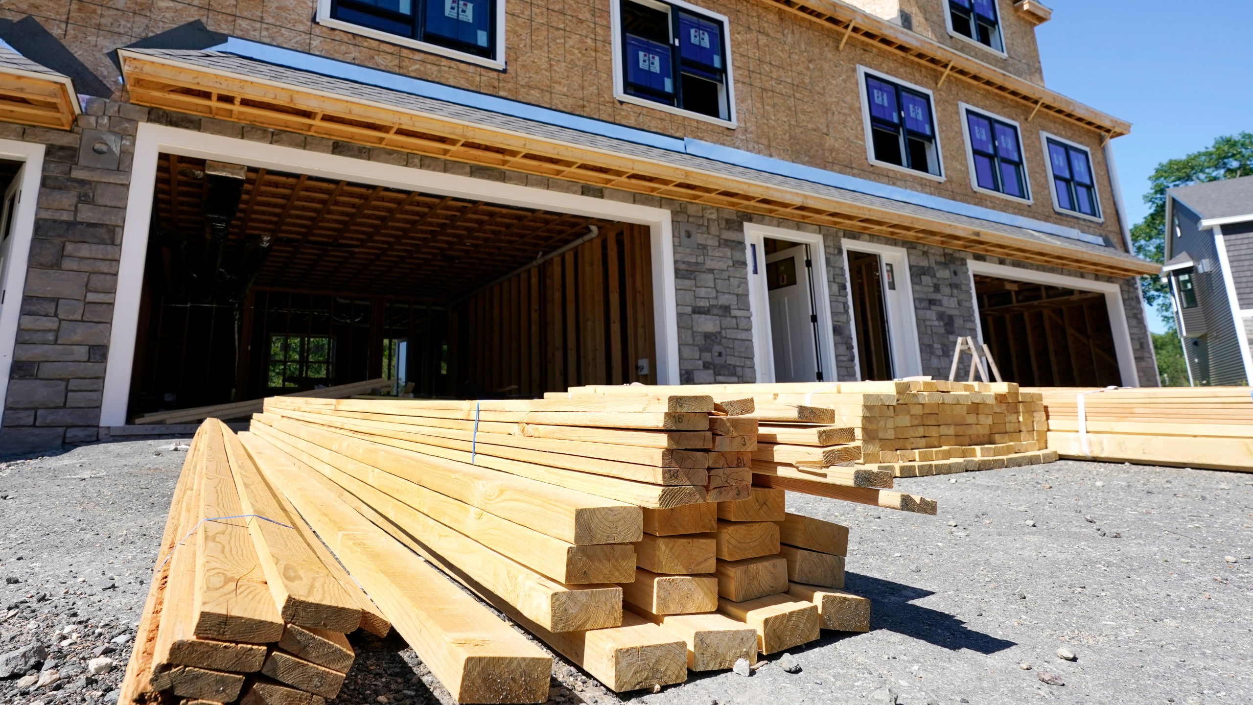 In this June 24, 2021 photo, lumber is piled at a housing construction site in Middleton, Mass. Rising costs and shortages of building materials and labor are rippling across the homebuilding industry, which accounted for nearly 12% of all U.S. home sales in July. Construction delays are common, prompting many builders to pump the brakes on the number of new homes they put up for sale. As building a new home gets more expensive, some of those costs are passed along to buyers. (AP Photo/Elise Amendola)