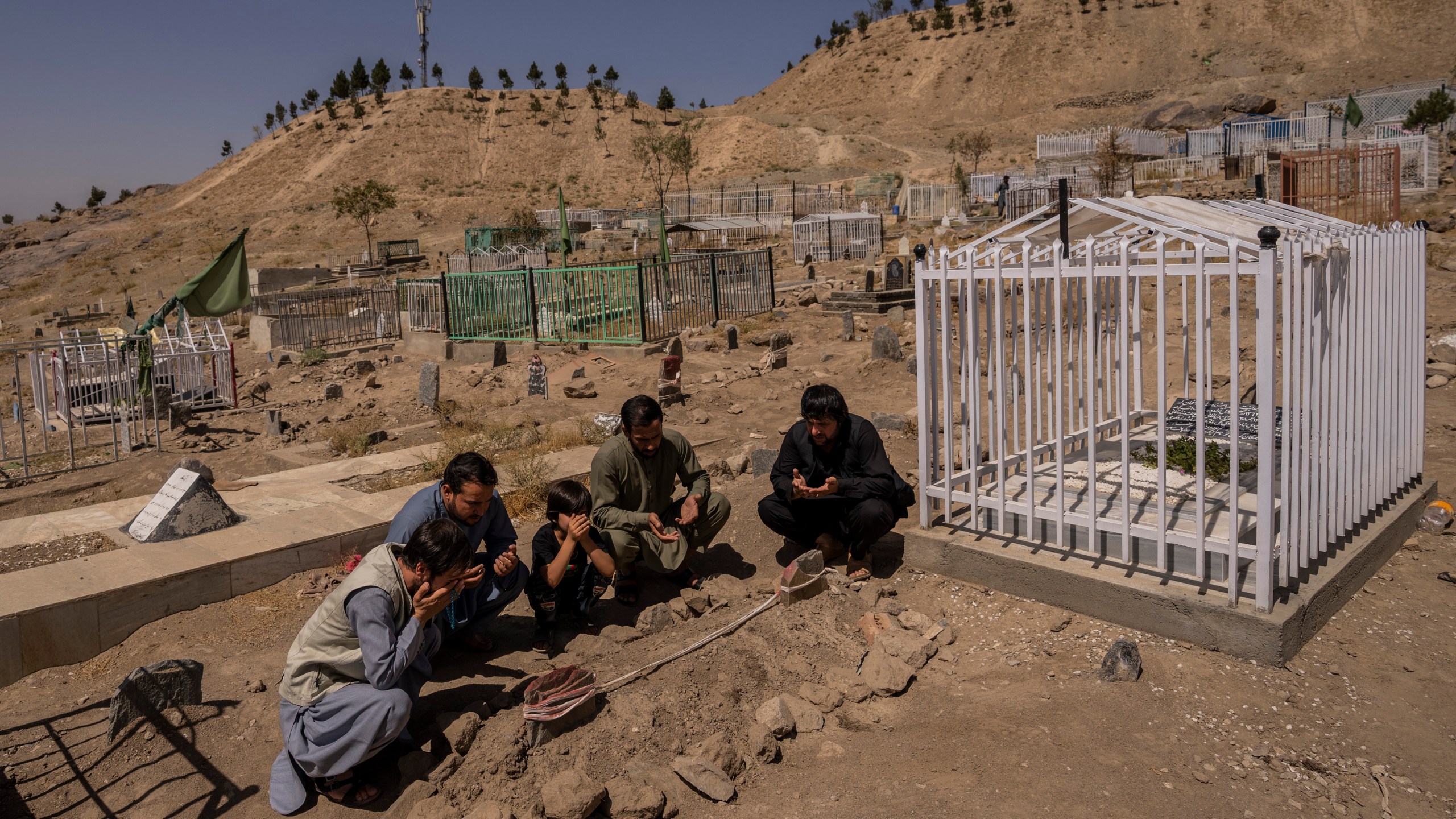 In this Monday, Sept. 13, 2021 file photo, the Ahmadi family pray at the cemetery next to family graves of family members killed by a US drone strike, in Kabul, Afghanistan. (AP Photo/Bernat Armangue, File)