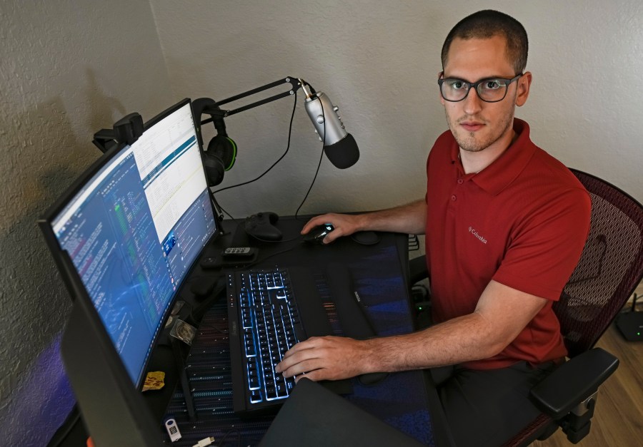 In this Sept. 20, 2021, photo Austin Moody poses for a photo as he sits a his home work station in Tampa, Fla. Moody, the Michigan native, got a scholarship from the Department of Defense that required working for the agency at least a year after graduating. (AP Photo/Steve Nesius)