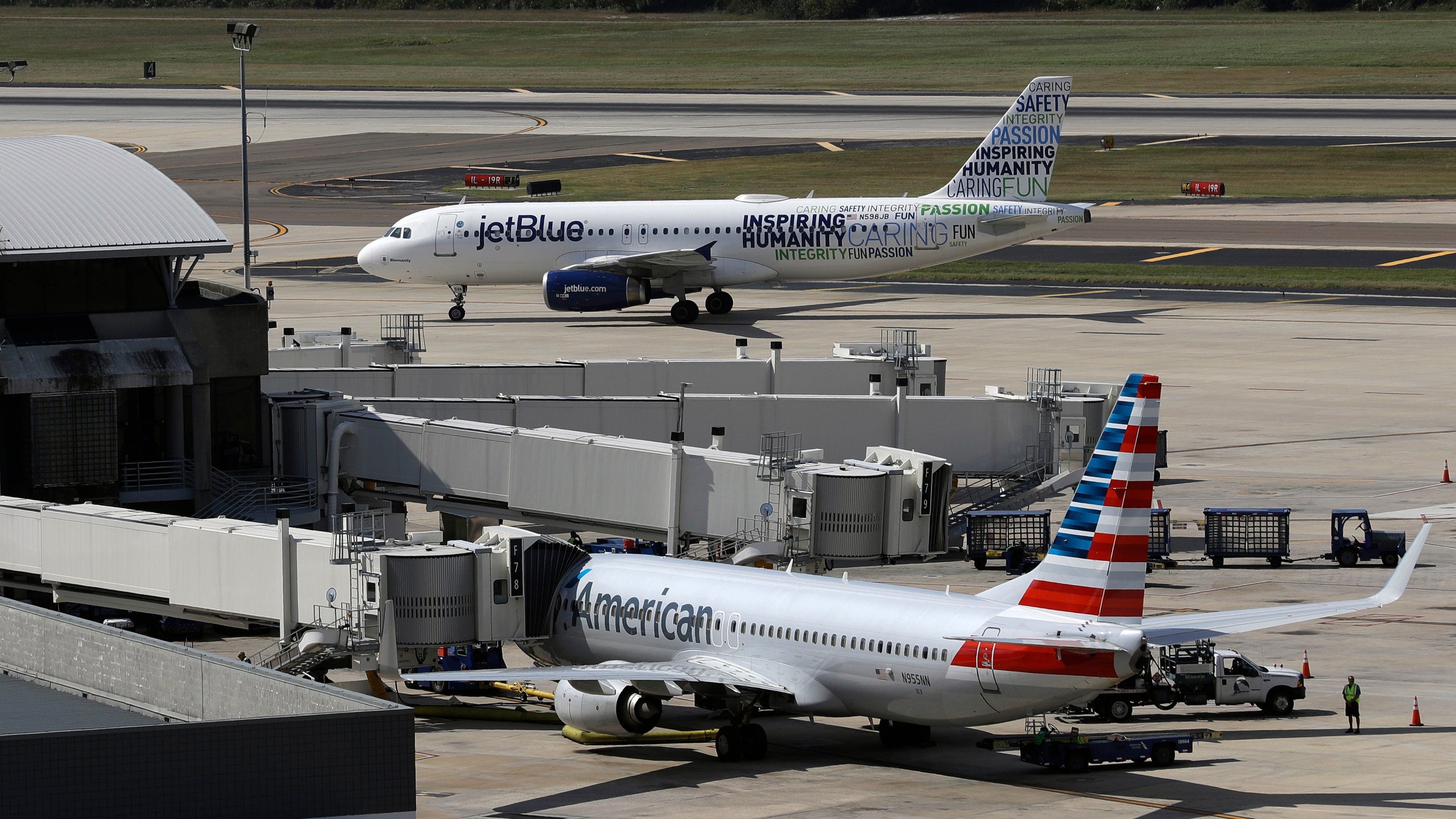 A JetBlue Airbus A320 taxis to a gate Wednesday, Oct. 26, 2016, after landing as an American Airlines jet is seen parked at its gate at Tampa International Airport in Tampa, Fla. (AP Photo/Chris O'Meara, File)