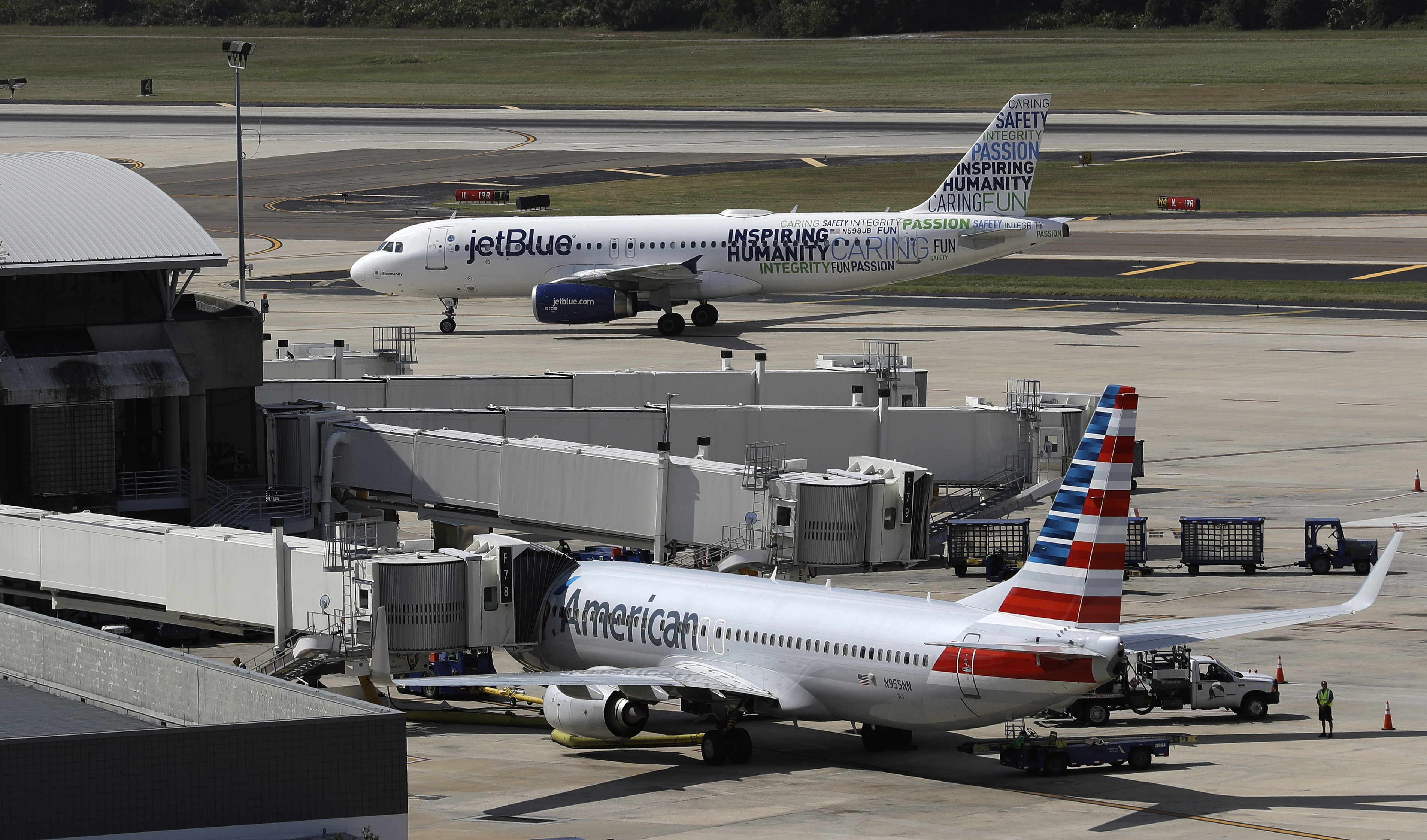 A JetBlue Airbus A320 taxis to a gate Wednesday, Oct. 26, 2016, after landing as an American Airlines jet is seen parked at its gate at Tampa International Airport in Tampa, Fla. (AP Photo/Chris O'Meara, File)