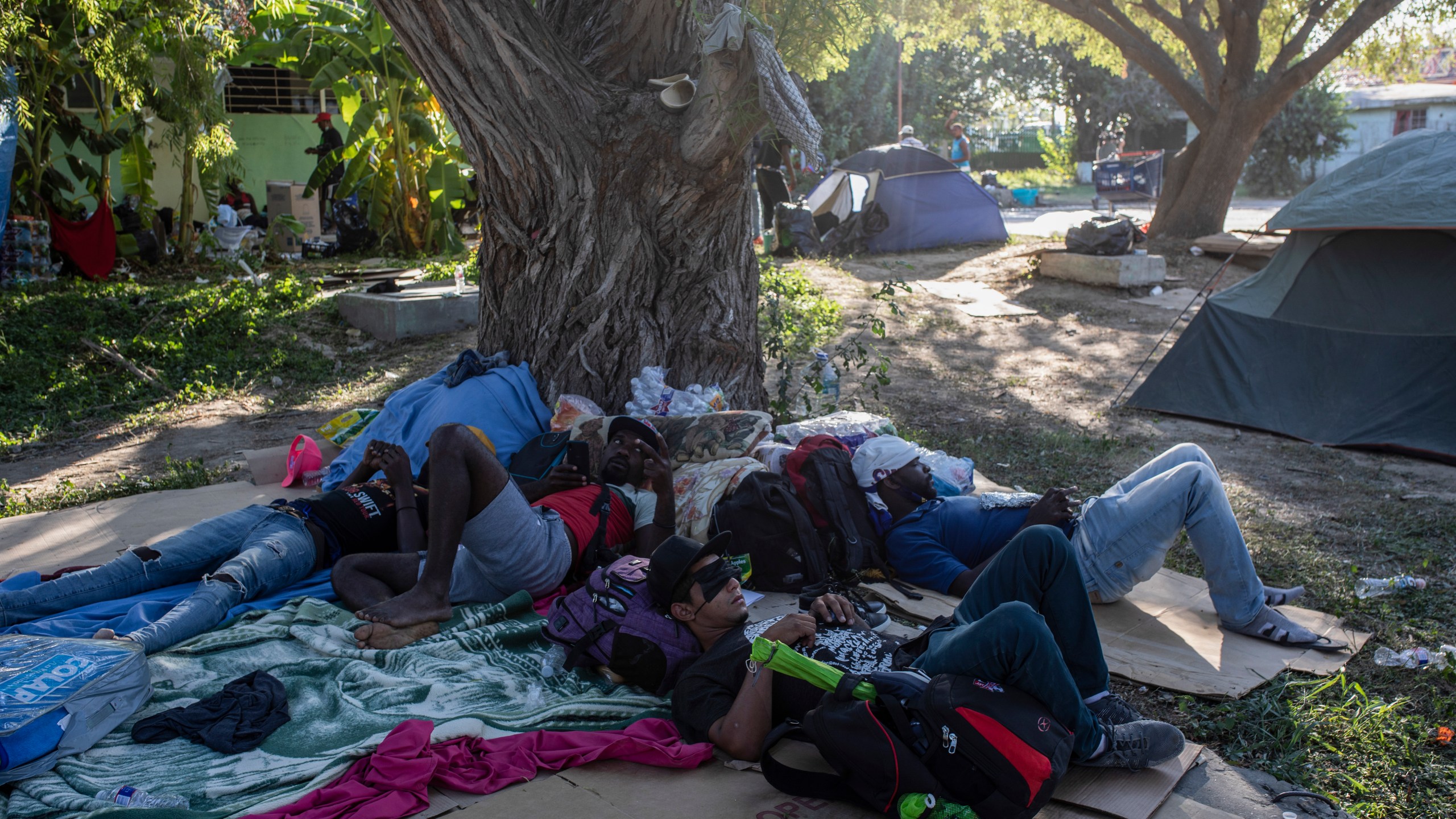 Migrants rest under the shade of a tree in Ciudad Acuna, Mexico, Friday, Sept. 24, 2021, across the Rio Grande from Del Rio, Texas. (AP Photo/Felix Marquez)