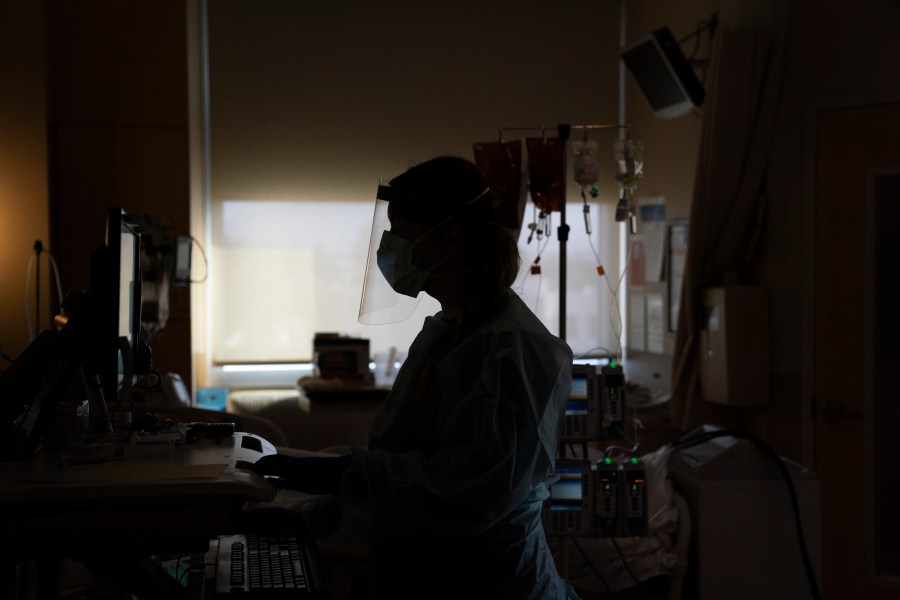 In this Nov. 19, 2020, file photo, a nurse works on a computer while assisting a COVID-19 patient at a hospital in Los Angeles. Across the country, doctors and nurses on the front lines of the coronavirus pandemic are dealing with hostility, threats and violence from patients angry over safety rules designed to keep the virus from spreading. (AP Photo/Jae C. Hong, File)