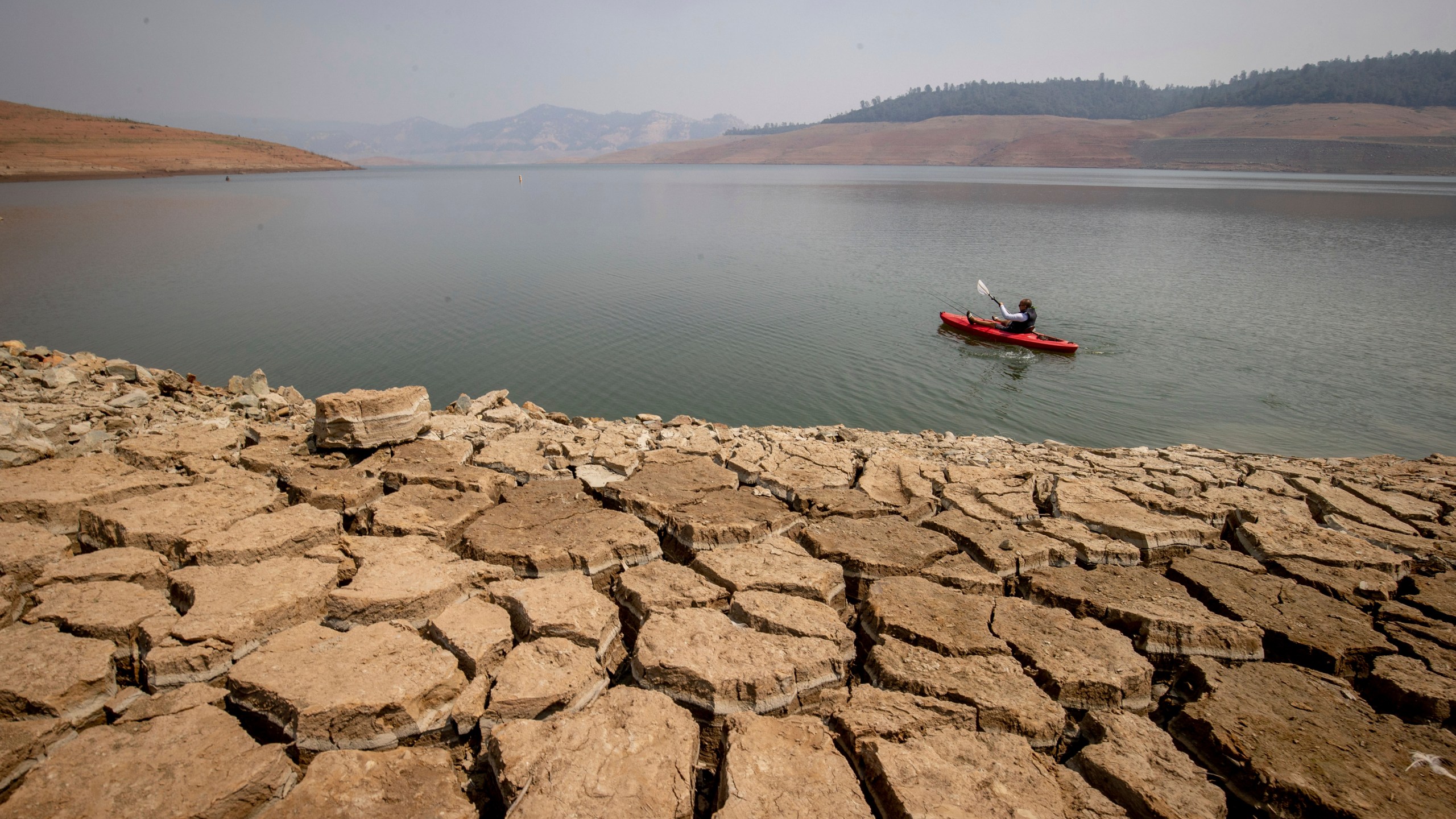 A kayaker fishes in Lake Oroville as water levels remain low due to continuing drought conditions on Aug. 22, 2021. (Ethan Swope / Associated Press)