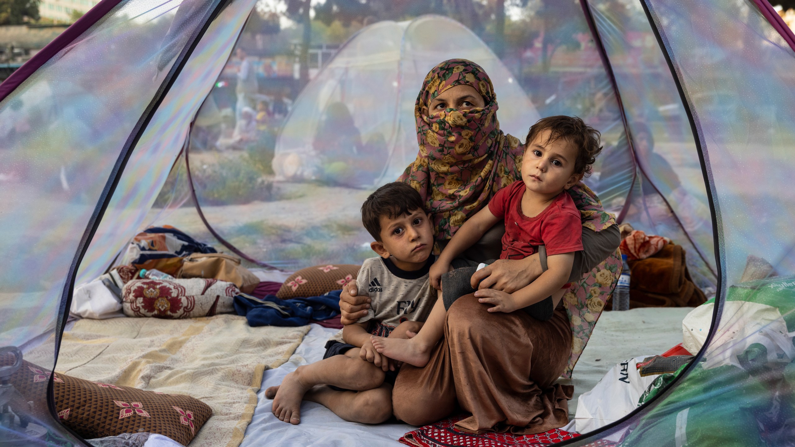 Farzia, 28, who lost her husband in Baghlan one week ago to fighting by the Taliban sits with her children, Subhan, 5, and Ismael ,2, in a tent at a makeshift IDP camp in Share-e-Naw park to various mosques and schools on August 12, 2021 in Kabul, Afghanistan. (Paula Bronstein/Getty Images)