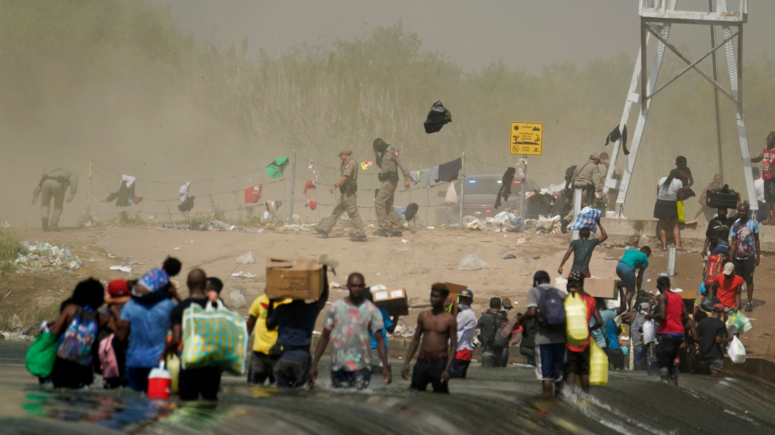 A dust storm moves across the area as Haitian migrants use a dam to cross into and from the United States from Mexico, Saturday, Sept. 18, 2021, in Del Rio, Texas. The U.S. plans to speed up its efforts to expel Haitian migrants on flights to their Caribbean homeland, officials said Saturday as agents poured into a Texas border city where thousands of Haitians have gathered after suddenly crossing into the U.S. from Mexico. (AP Photo/Eric Gay)