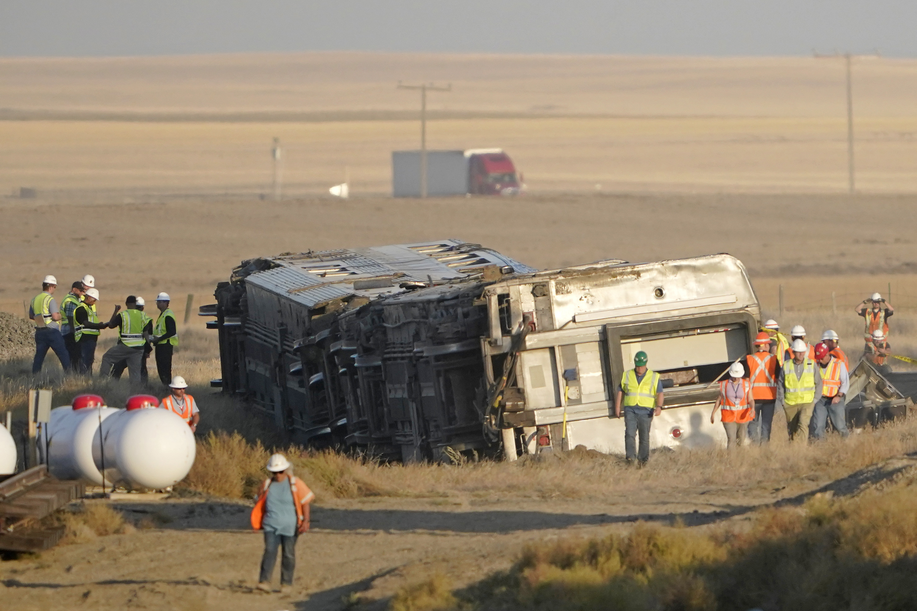 Workers stand Sunday, Sept. 26, 2021, near toppled cars from an Amtrak train that derailed Saturday, just west of Joplin, Mont. The westbound Empire Builder was en route to Seattle from Chicago with two locomotives and 10 cars. (AP Photo/Ted S. Warren)