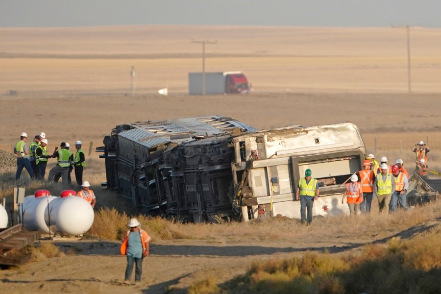 Workers stand Sunday, Sept. 26, 2021, near toppled cars from an Amtrak train that derailed Saturday, just west of Joplin, Mont. The westbound Empire Builder was en route to Seattle from Chicago with two locomotives and 10 cars. (AP Photo/Ted S. Warren)