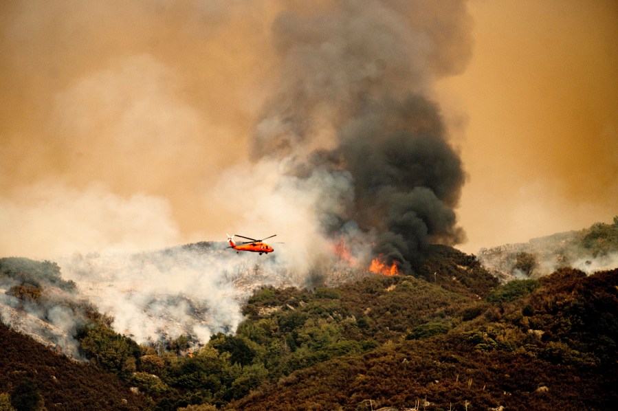 A helicopter prepares to drop water on the KNP Complex Fire in Sequoia National Park, Calif., on Wednesday, Sept. 15, 2021. The blaze is burning near the Giant Forest, home to more than 2,000 giant sequoias. (AP Photo/Noah Berger)