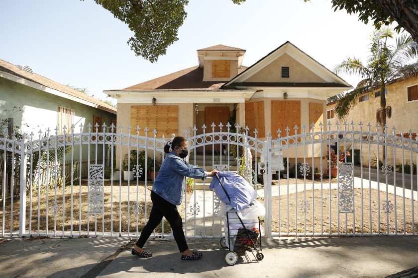 A woman walks past a boarded-up home on East 27th Street in South L.A. in August 2021. (Al Seib / Los Angeles Times)