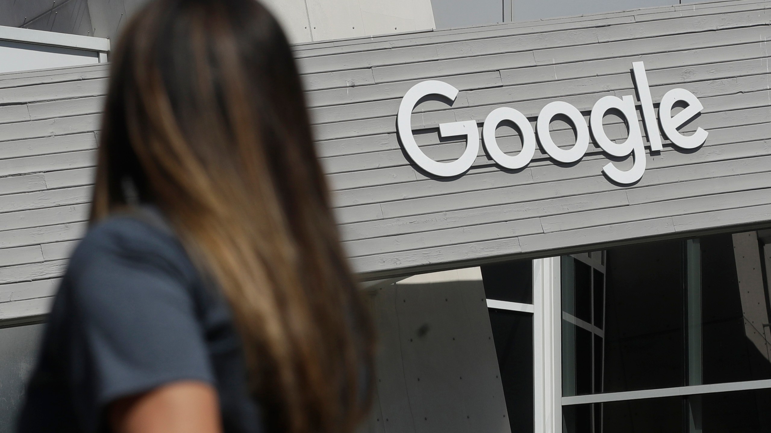 In this Sept. 24, 2019, file photo, a woman walks below a Google sign on the campus in Mountain View, Calif. Google on Thursday, Oct. 7, 2021, will no longer allow digital ads promoting false climate change claims to appear next to the content of other publishers, hoping to deny money to those making such claims and to stop the spread of misinformation on its platform. (AP Photo/Jeff Chiu, File)