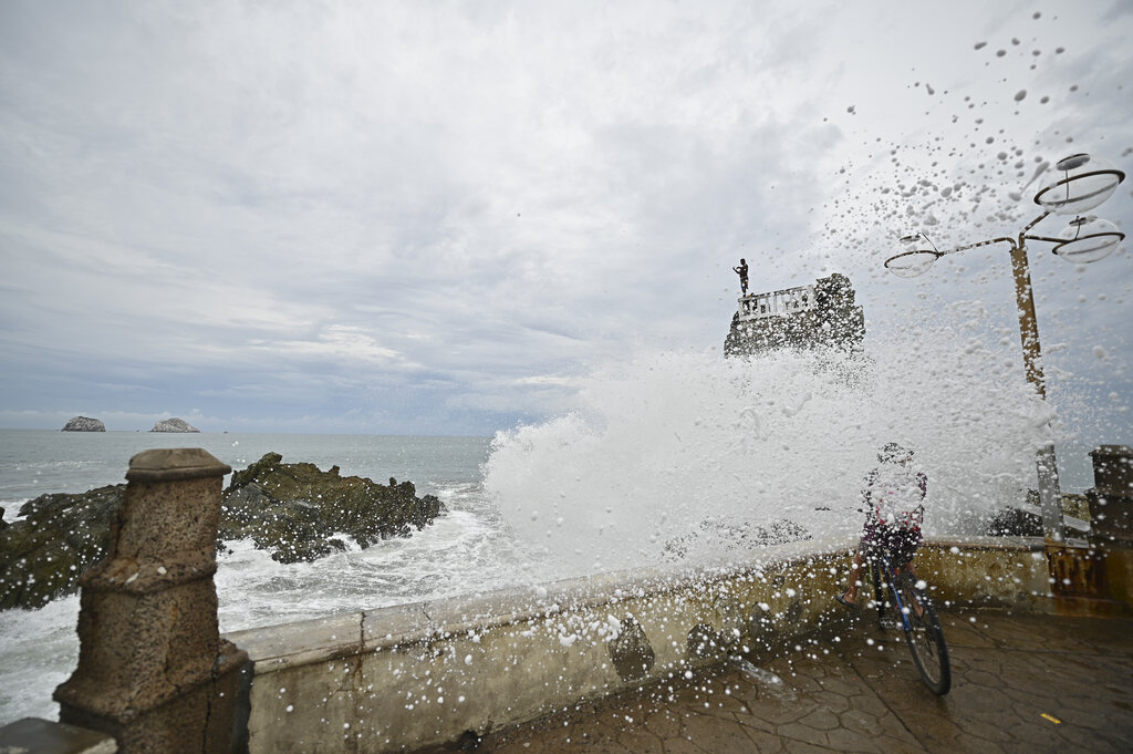 A cyclist is splashed by a crashing wave prior the landfall of tropical storm Pamela, on the boardwalk in Mazatlan, Mexico, Tuesday, Oct. 12, 2021. (AP Photo/Roberto Echeagaray)