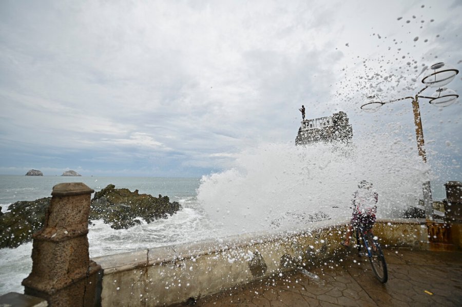 A cyclist is splashed by a crashing wave prior the landfall of tropical storm Pamela, on the boardwalk in Mazatlan, Mexico, Tuesday, Oct. 12, 2021. (AP Photo/Roberto Echeagaray)