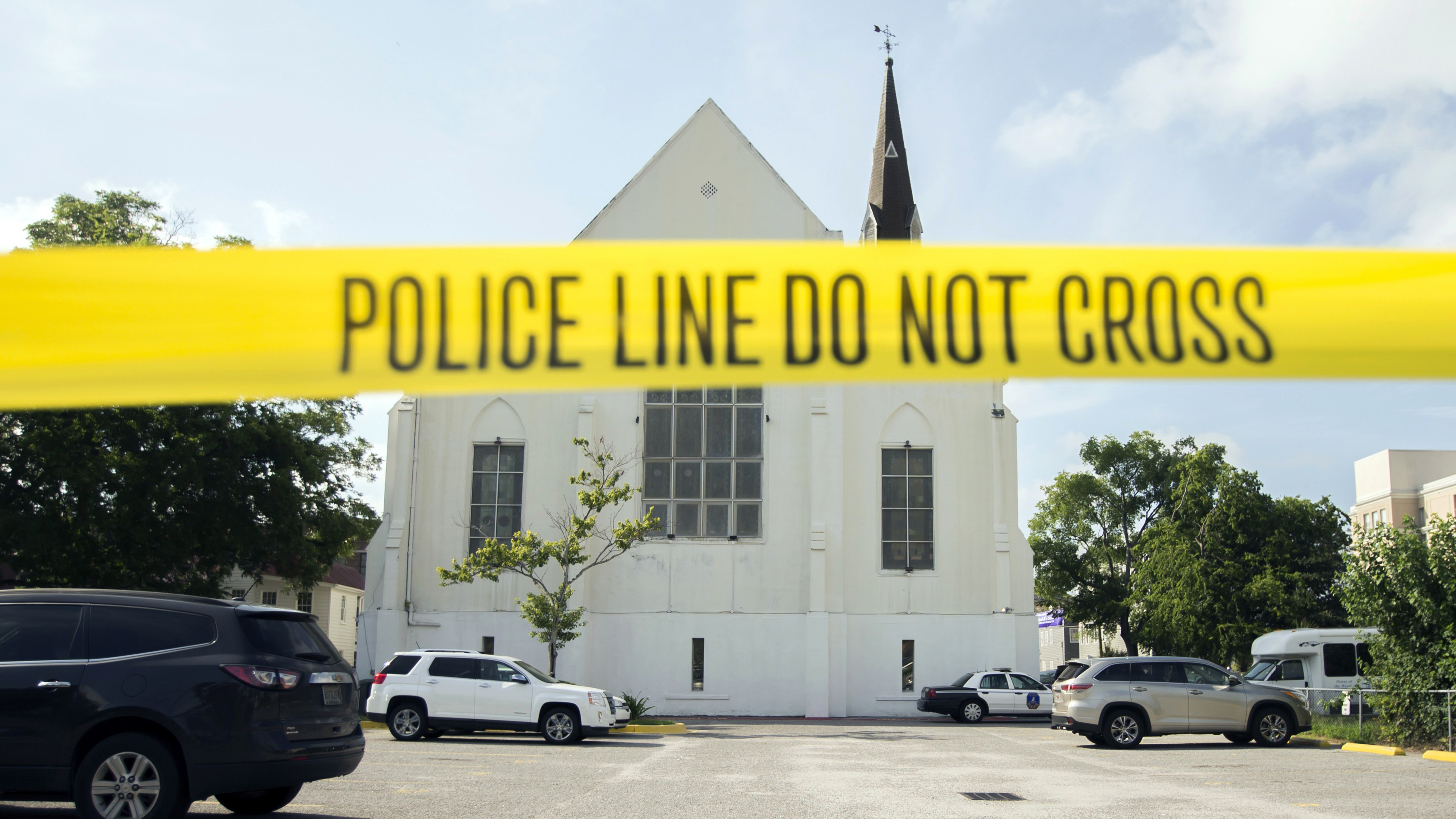 In this June 19, 2015 file photo, police tape surrounds the parking lot behind the AME Emanuel Church as FBI forensic experts work the crime scene, in Charleston, S.C. Families of nine victims killed in a racist attack at the church have reached a settlement with the Justice Department over a faulty background check that allowed Dylann Roof to purchase the gun he used in the 2015 massacre. (AP Photo/Stephen B. Morton, File)