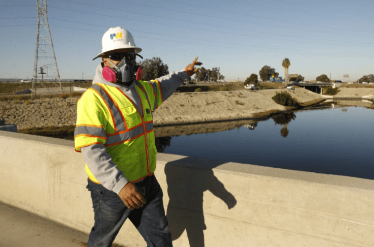 A crew member from the Los Angeles County Department of Public Works, wearing a mask to block out the noxious smell, prepares to work on the Dominguez Channel in Carson.(Carolyn Cole / Los Angeles Times)