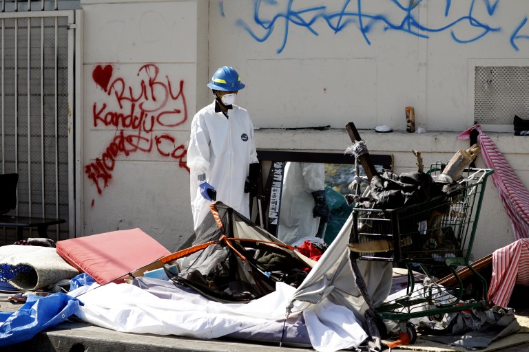 An L.A. sanitation worker cleans up around a homeless encampment on a sidewalk in South Los Angeles in 2018. (Francine Orr / Los Angeles Times)