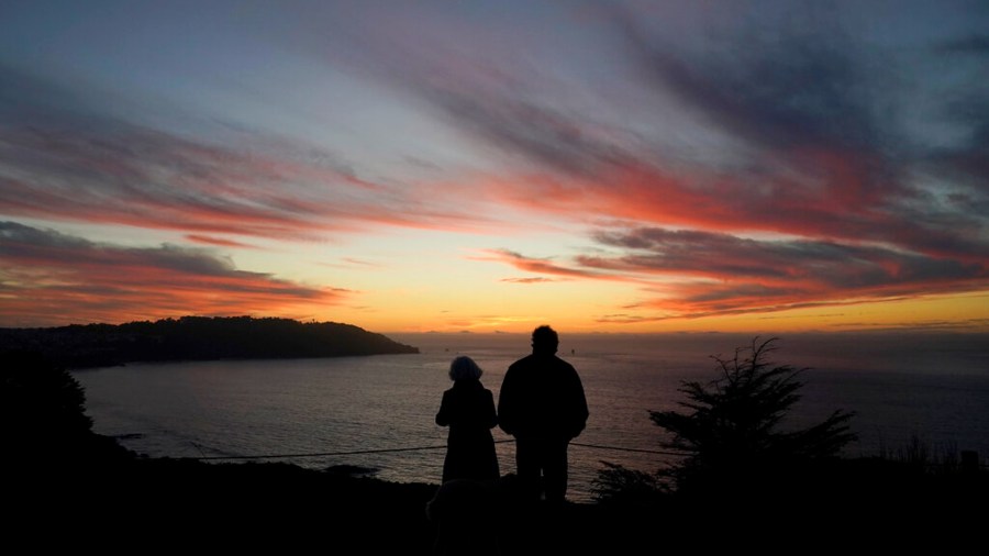 In this Dec. 21, 2020, file photo people watch as the sun sets from the Presidio in San Francisco. (AP Photo/Jeff Chiu, File)