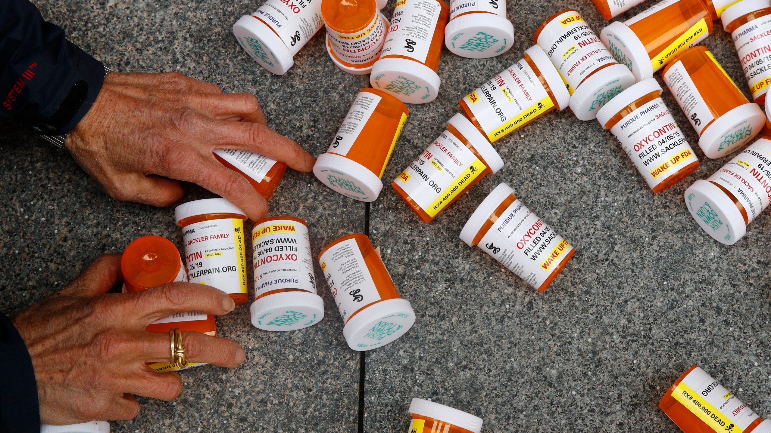 A protester gathers containers that look like OxyContin bottles at an anti-opioid demonstration in front of the U.S. Department of Health and Human Services headquarters in Washington on April 5, 2019. A California judge has ruled for top drug manufacturers as local governments seek billions of dollars to cover their costs from the nation’s opioid epidemic. Orange County Superior Court Judge Peter Wilson issued a tentative ruling Monday, Nov. 1, 2021, that said the governments hadn't proven the pharmaceutical companies used deceptive marketing to increase unnecessary opioid prescriptions and create a public nuisance. (AP Photo/Patrick Semansky, File)