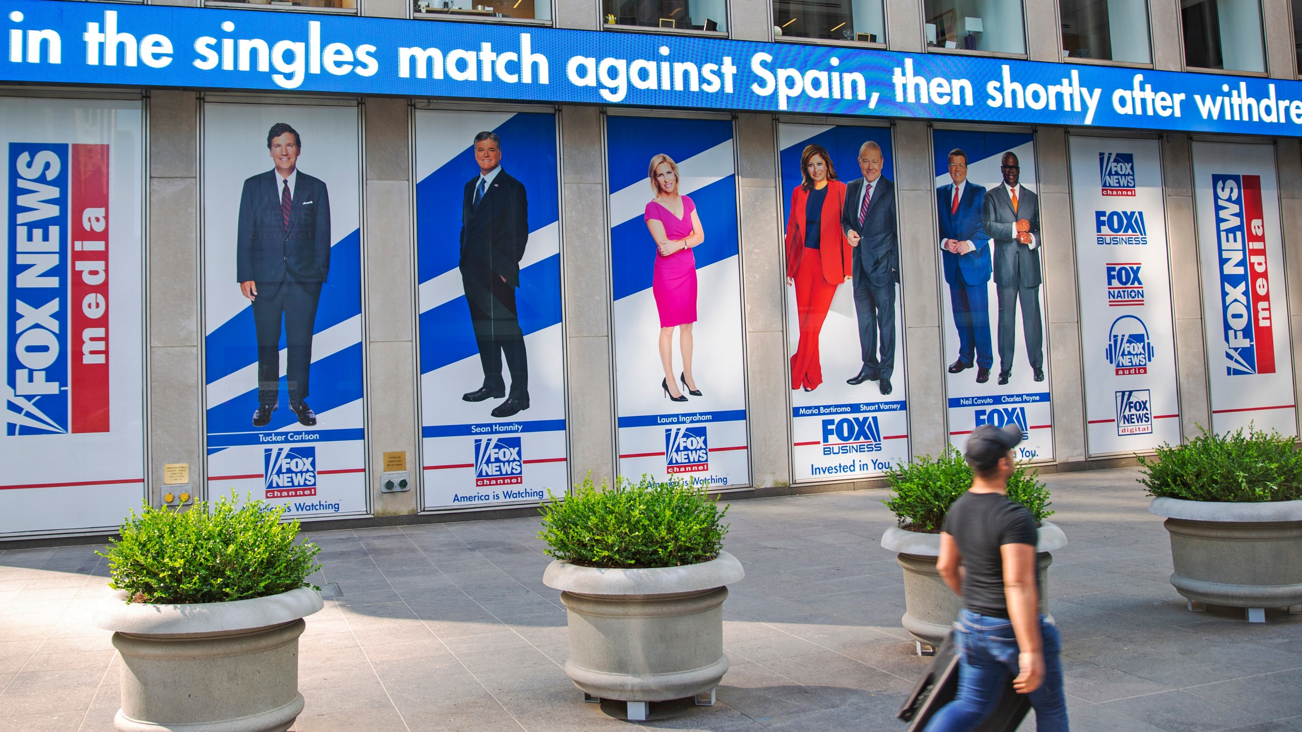 A man walks past promotional posters outside Fox News studios at News Corporation headquarters in New York on Saturday, July 31, 2021. From left to right are hosts Tucker Carlson, Sean Hannity, Laura Ingraham, Maria Bartiromo, Stuart Varney, Neil Cavuto and Charles Payne. (AP Photo/Ted Shaffrey, File)