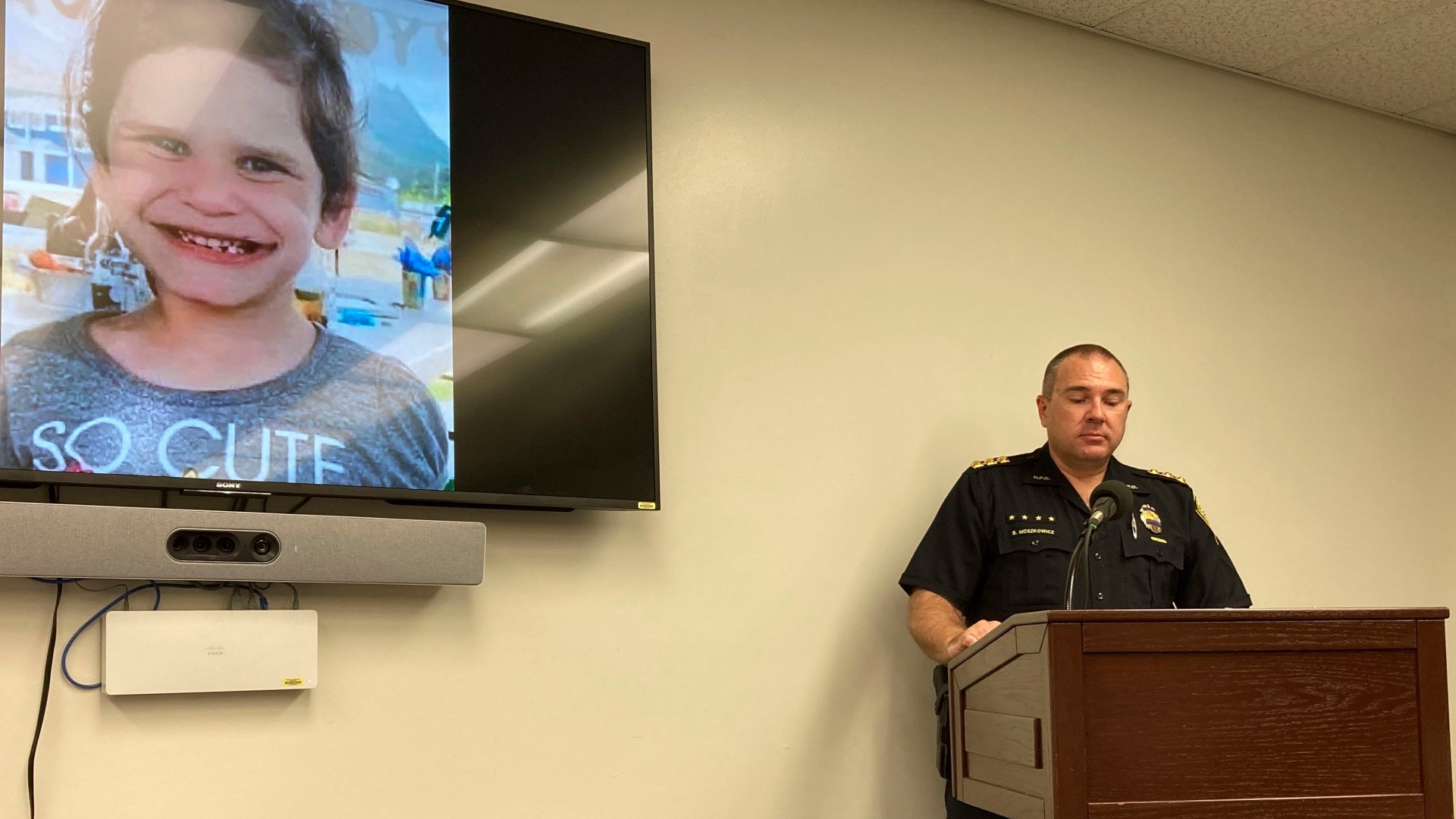 Honolulu Police Maj. Ben Moszkowicz addresses a news conference in Honolulu on Wednesday, Nov. 10, 2021, where law enforcement officers said they arrested the adopted parents of Isabella "Ariel" Kalua, shown on the screen to the left. The parents, Lehua and Isaac "Sonny" Kalua have been charged with second-degree murder in the girl's death. Police say the girl was killed a month before they reported her missing Sept. 13, 2021. (AP Photo/Jennifer Sinco Kelleher)