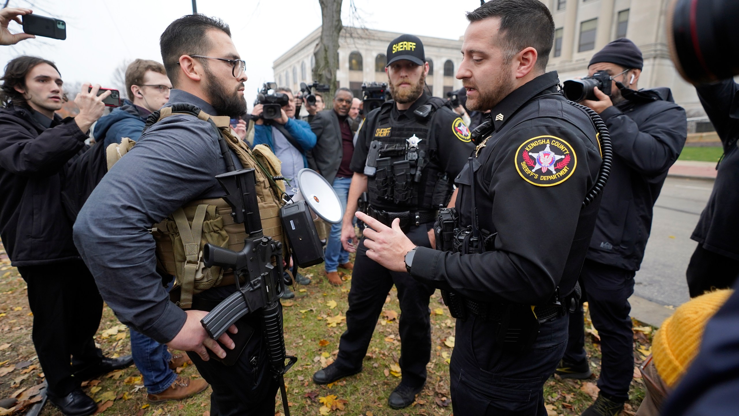 Kenosha County Sheriffs Department officers question a protester carrying a rifle outside the Kenosha County Courthouse, Wednesday, Nov. 17, 2021 in Kenosha, Wis., during the Kyle Rittenhouse murder trial. Rittenhouse is accused of killing two people and wounding a third during a protest over police brutality in Kenosha, last year. (AP Photo/Paul Sancya)