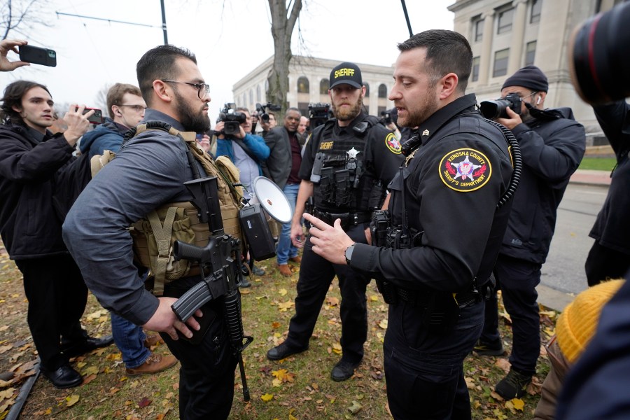 Kenosha County Sheriffs Department officers question a protester carrying a rifle outside the Kenosha County Courthouse, Wednesday, Nov. 17, 2021 in Kenosha, Wis., during the Kyle Rittenhouse murder trial. Rittenhouse is accused of killing two people and wounding a third during a protest over police brutality in Kenosha, last year. (AP Photo/Paul Sancya)