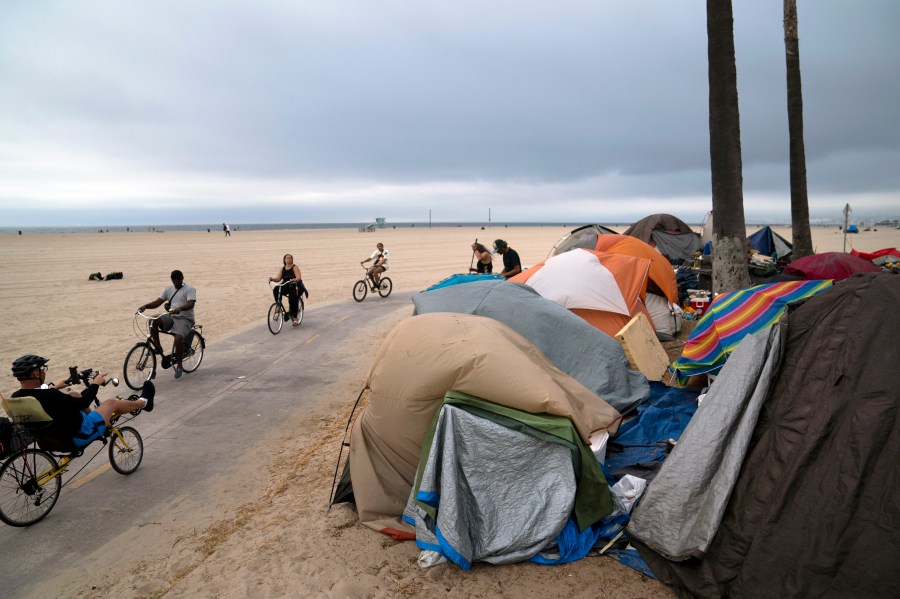 People ride their bikes past a homeless encampment set up along the boardwalk in the Venice neighborhood of Los Angeles on June 29, 2021. (AP Photo/Jae C. Hong, File)