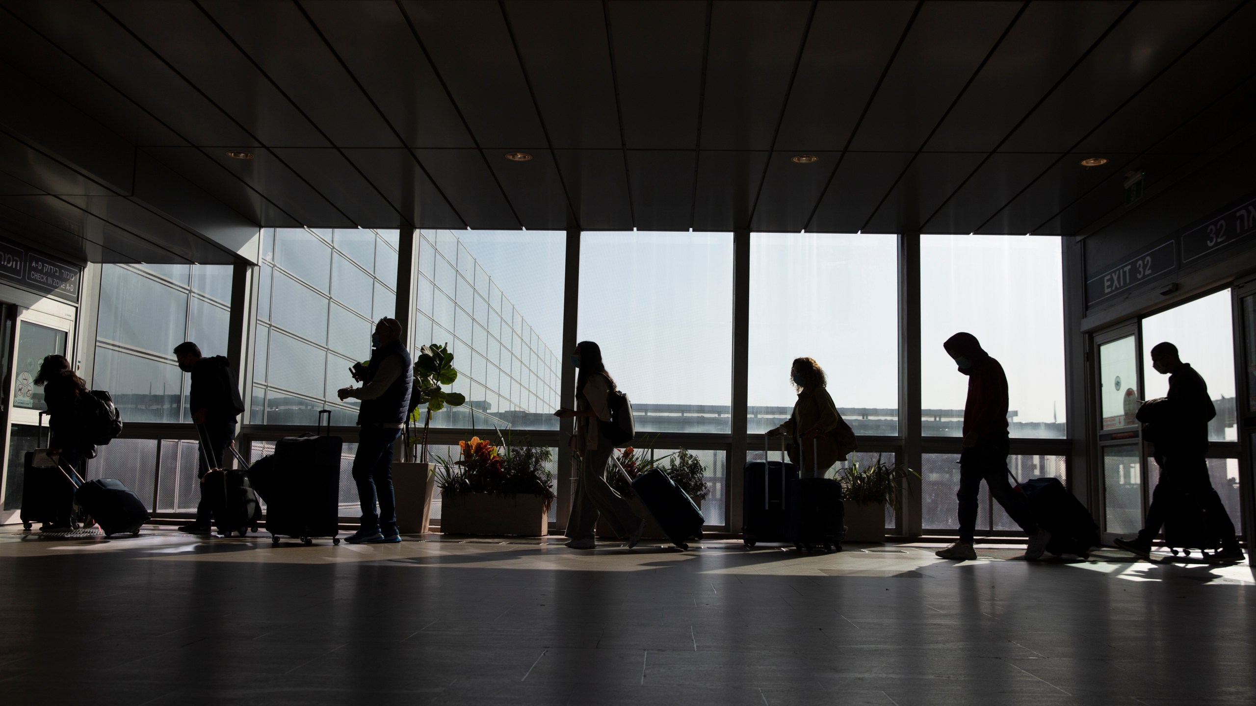 Travelers walk with their luggage in the Ben Gurion Airport near Tel Aviv, Israel, Sunday, Nov. 28, 2021. Israel on Sunday approved barring entry to foreign nationals and the use of controversial technology for contact tracing as part of its efforts to clamp down on a new coronavirus variant. (AP Photo/Ariel Schalit)