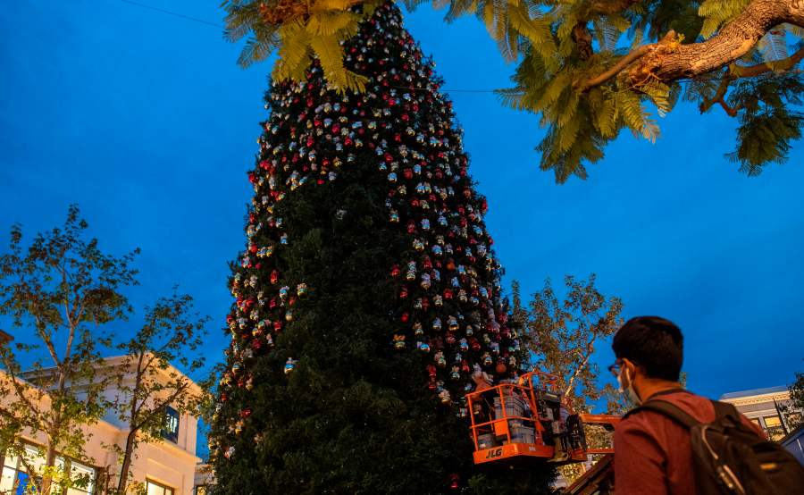 A person wearing a face mask watches a worker decorate the Christmas tree at The Grove outdoor shopping center, amid the coronavirus pandemic on Nov. 5 2020. (VALERIE MACON via Getty Images)