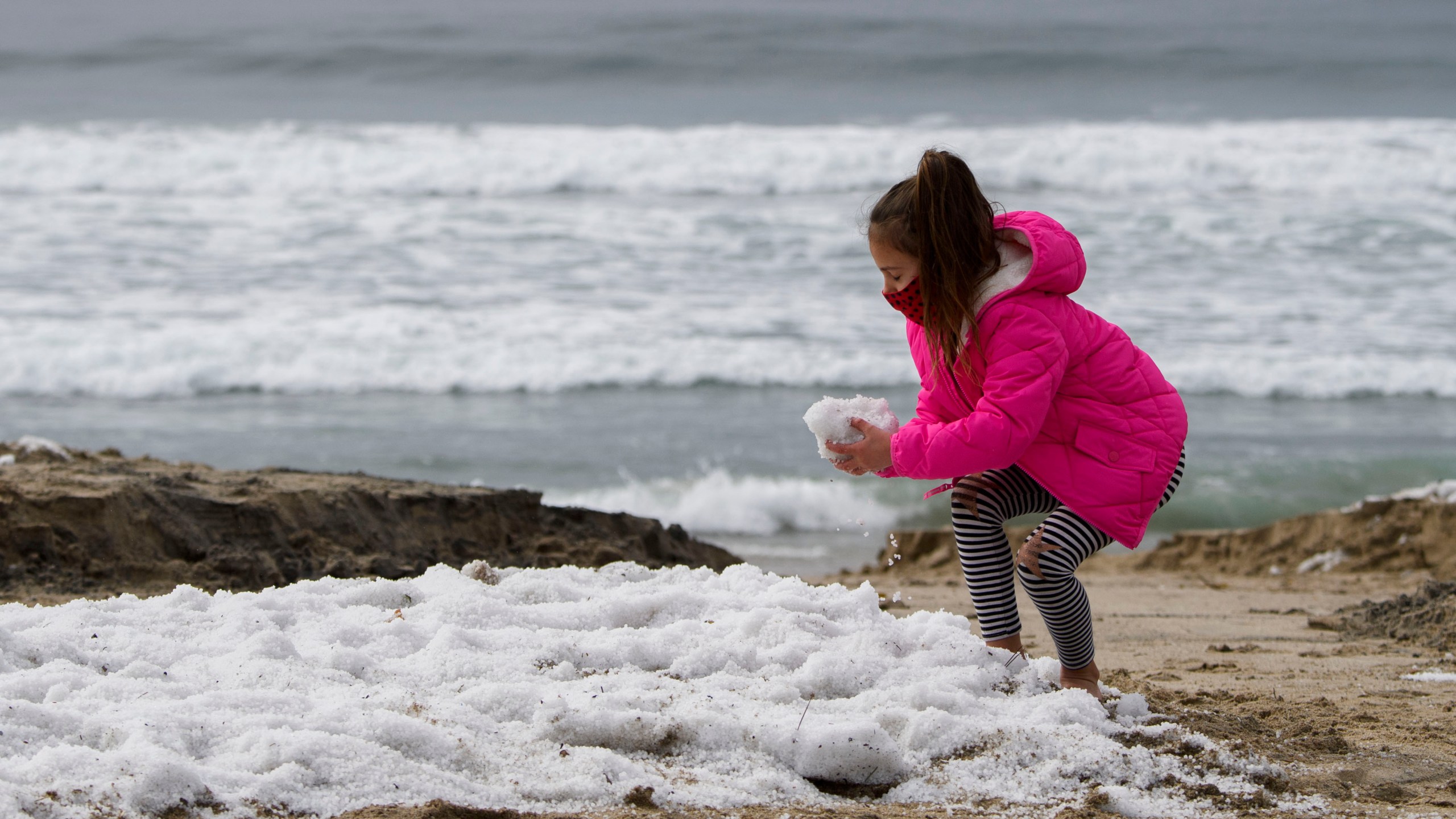 A girl plays with hail on the beach following winter storms that blanketed the region with rain, snow and hail, on Jan. 29, 2021, in Manhattan Beach, California. (PATRICK T. FALLON/AFP via Getty Images)