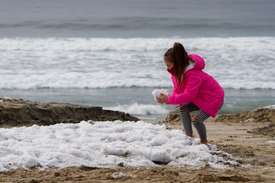 A girl plays with hail on the beach following winter storms that blanketed the region with rain, snow and hail, on Jan. 29, 2021, in Manhattan Beach, California. (PATRICK T. FALLON/AFP via Getty Images)