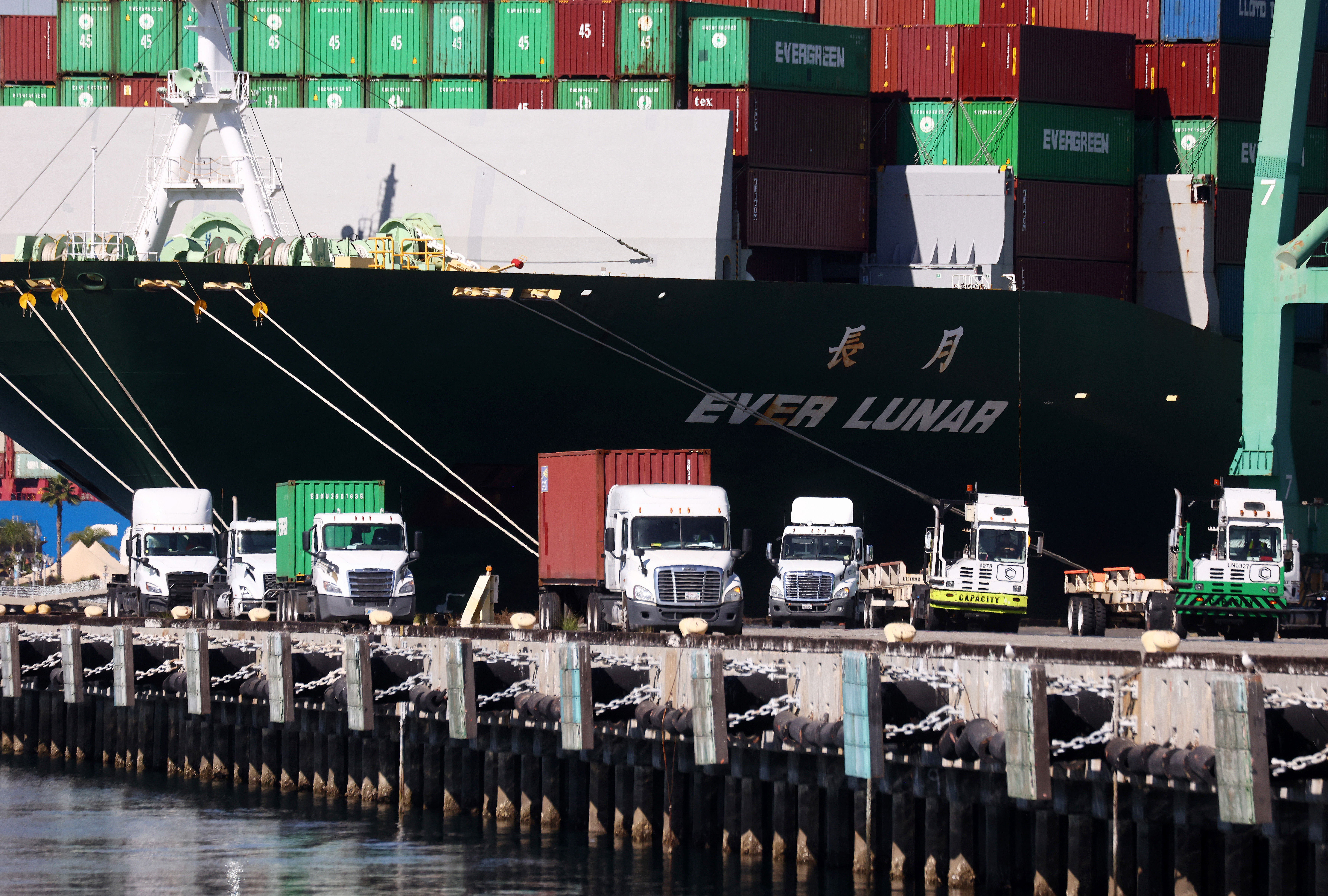 Trucks drive beneath cargo containers stacked on a container ship at the Port of Los Angeles on Oct. 15, 2021 in San Pedro. (Mario Tama/Getty Images)