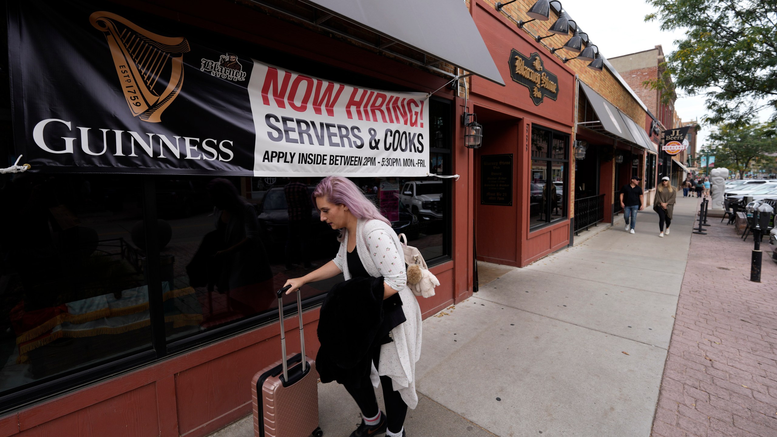 A traveller wheels her baggage past a now hiring sign outside a bar and restaurant Saturday, Oct. 9, 2021, in Sioux Falls, S.D. America’s employers slowed the pace of their hiring in November, adding 210,000 jobs, the lowest monthly gain in nearly a year. Friday, Dec. 3 report from the Labor Department also showed that the nation's unemployment rate tumbled from 4.6% to 4.2% evidence that many more people reported that they had a job. (AP Photo/David Zalubowski)