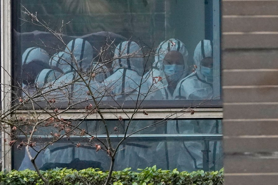 FILE - Members of a World Health Organization team are seen through a window wearing protective gear during a field visit to the Hubei Animal Disease Control and Prevention Center for another day of field visit in Wuhan in central China's Hubei province, on Feb. 2, 2021. Nearly two years into the COVID-19 pandemic, the origin of the virus tormenting the world remains shrouded in mystery. (AP Photo/Ng Han Guan, File)