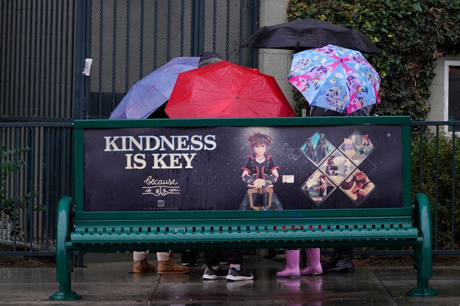 People huddle under their umbrellas at a bus stop downtown Los Angeles on Dec. 14, 2021. (Damian Dovarganes/Associated Press)